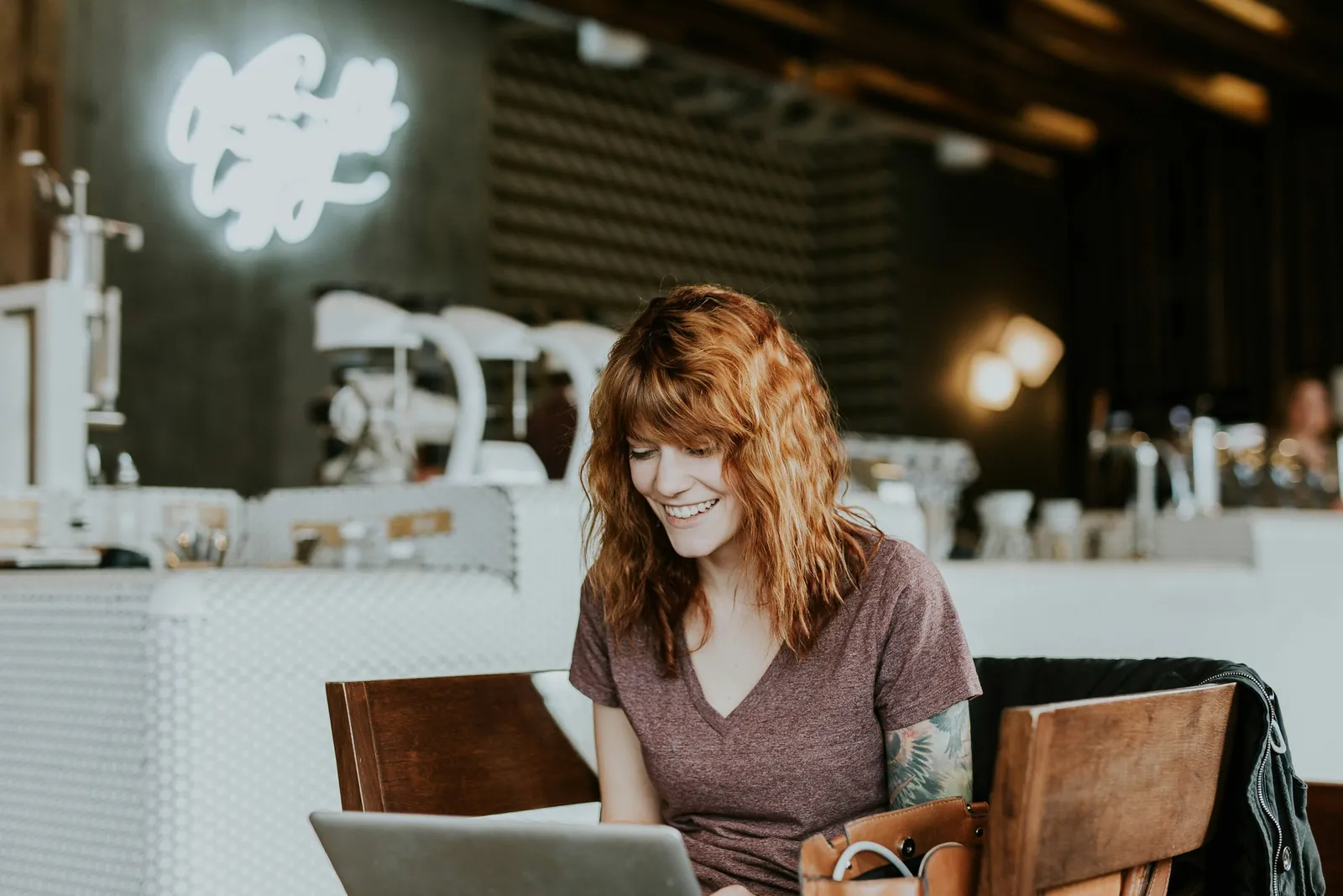 Woman smiling while working on a laptop in a café